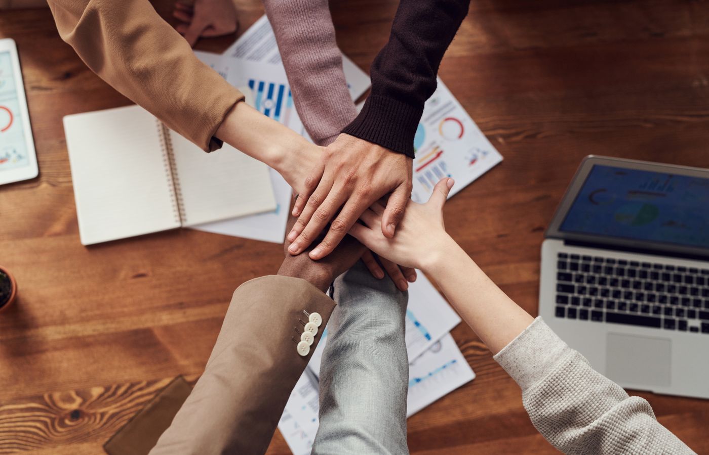 Colleagues stacking their hands above a meeting table, illustrating teamwork